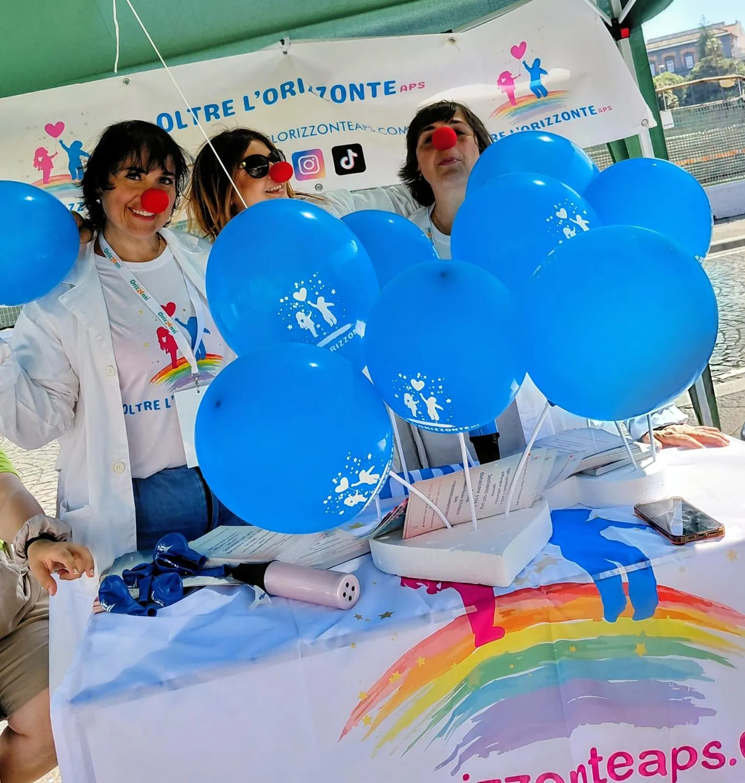 Volontarie con palloncini celesti e nasi rossi allo stand di Oltre l’Orizzonte APS